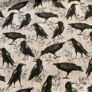 Puede incluir: Una tela con un patrón repetido de cuervos negros sobre un fondo gris claro con un sutil diseño de hojas. Los cuervos se representan en varias poses, creando un textil dinámico y visualmente interesante.