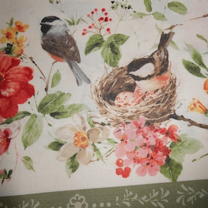 Può includere: Un tessuto bianco con un motivo floreale con fiori rossi, rosa e arancioni. Sono raffigurati due uccelli, uno appollaiato su un ramo e l'altro in un nido.