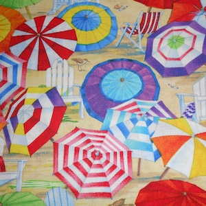 Op de afbeelding: Een kleurrijke strandscène met talrijke open parasols in verschillende kleuren en patronen, waaronder rood, wit, blauw, geel en paars. Witte Adirondack-stoelen en strandstoelen zijn verspreid over het zand.