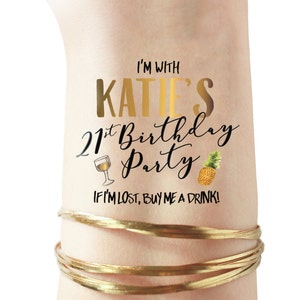 May include: A temporary tattoo with gold lettering that says "I'm with Katie's 21st Birthday Party" with a glass of wine and a pineapple graphic. The text below the main text says "If I'm lost, buy me a drink!"