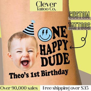 May include: A temporary tattoo featuring a smiling baby wearing a party hat. The tattoo reads "ONE HAPPY DUDE" with "Theo's 1st Birthday" below. The words "Clever Tattoo Co." and "CUSTOM TATTOOS" are also visible.