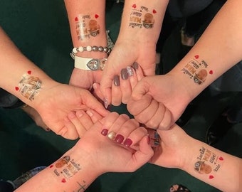 Könnte beinhalten: Nahaufnahme von vier Armen mit temporären Tattoos, auf denen "Luckiest Mom Alive!" und "Luckiest Dad Alive!" steht, sowie ein Bild eines Mannes in Militäruniform. Die Tattoos sind in Rot, Schwarz und Weiß.