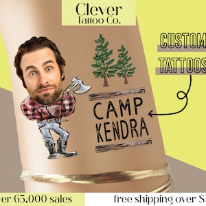 May include: A brown arm with a temporary tattoo of a cartoon lumberjack holding an axe, two pine trees, and a wooden sign that says "Camp Kendra". The text "Custom Tattoos" is written in black on a yellow background.