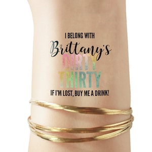 May include: A temporary tattoo with the text "I belong with Brittany's Dirty Thirty. If I'm lost, buy me a drink!" in black text. The words "Dirty Thirty" are in rainbow colors.