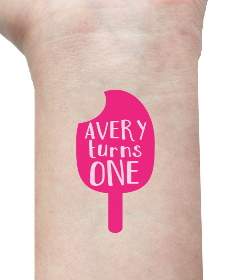 Puede incluir: Tatuaje temporal en forma de paleta de helado rosa con el texto "Avery turns one" en la mu&ntilde;eca de una persona.