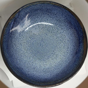 Può includere: Una ciotola in ceramica blu con una glassa macchiettata. La ciotola ha un bordo blu scuro e un interno blu chiaro.