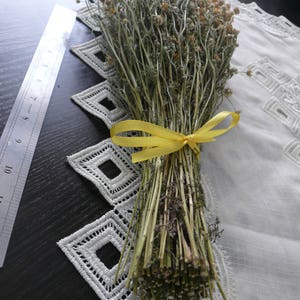 Puede incluir: Un manojo de flores de manzanilla secas atadas con una cinta amarilla. Las flores est&aacute;n dispuestas sobre un mantel de encaje blanco.