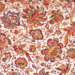 Può includere: Una tenda in tessuto bianco con un motivo floreale rosso, arancione, giallo e blu. La tenda ha occhielli lungo il bordo superiore.