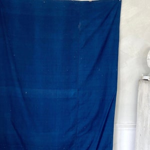 Op de afbeelding: Een groot, diepblauw stoffen paneel hangt aan een witte muur. De stof heeft een licht getextureerd oppervlak en is afgewerkt met een dunne rode bies.