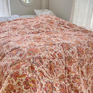 Può includere: Un grande trapunta di colore rosso e crema con motivo floreale e design trapuntato. La trapunta è piegata a metà e si trova su un letto.