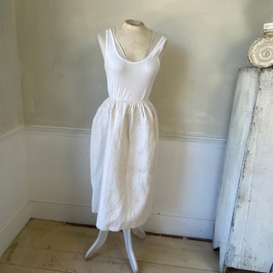 May include: A white linen skirt with a gathered waist, displayed on a white mannequin against a white wall.