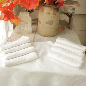 May include: A white linen tablecloth with embroidered napkins, a rustic stoneware crock, and a bouquet of red maple leaves.