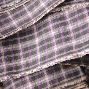 Pode incluir: Close-up de um tecido dobrado com um padrão xadrez em tons de roxo, preto e branco.