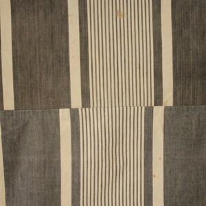 May include: A close-up of a striped fabric with alternating white and dark gray stripes. The fabric is made of a woven material and has a slightly textured surface.