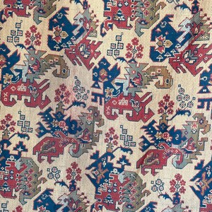 Könnte beinhalten: Ein beigefarbener Stoff mit einem sich wiederholenden Muster aus stilisierten Drachen in Rot, Blau und Gold. Die Drachen sind von kleineren geometrischen Formen und floralen Motiven umgeben.