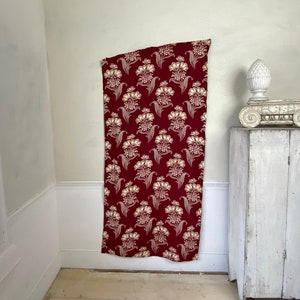 May include: A burgundy fabric with a white floral pattern. The fabric is hanging on a white wall in a room with white trim and a white wooden cabinet.
