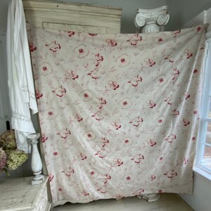 May include: A large piece of fabric with a floral pattern. The fabric is white with a red floral design. The fabric is hanging on a wall.