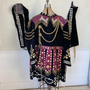 May include: A black velvet costume with gold and silver embellishments. The costume features a long skirt with a pink and gold trim. The costume is decorated with silver and gold buttons.