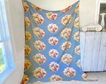 May include: A blue fabric with a floral pattern. The fabric features a repeating design of bouquets of pink, red, and yellow flowers in a white scalloped frame.