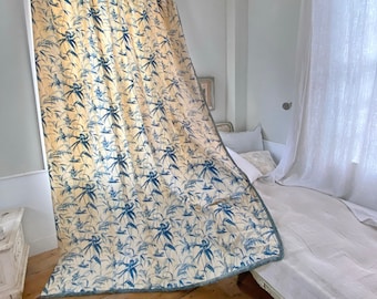 May include: A white and blue patterned curtain with a floral design hangs in a room with a white bed and white curtains. The curtain is made of a lightweight fabric and has a subtle sheen.