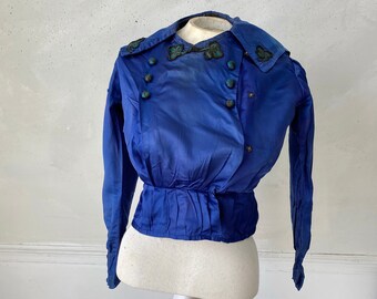 May include: A vintage cobalt blue jacket with a double-breasted design. The jacket features a wide collar, long sleeves, and decorative buttons. The collar and upper chest are adorned with embroidered embellishments. The jacket is displayed on a mannequin.