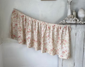 Könnte beinhalten: Eine weiße Gardine mit einem roten und cremefarbenen Blumenmuster. Die Gardine hängt an einer weißen Wand und bedeckt teilweise einen weißen Schrank.