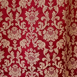 Könnte beinhalten: Roter Stoff mit einem goldenen Damastmuster. Das Muster zeigt komplizierte florale Designs und Wirbel.