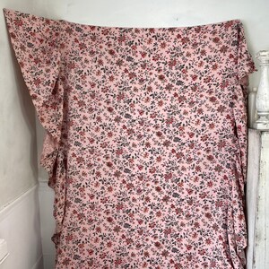 May include: A pink fabric with a small floral print in shades of red, brown, and black. The fabric has a ruffled edge.