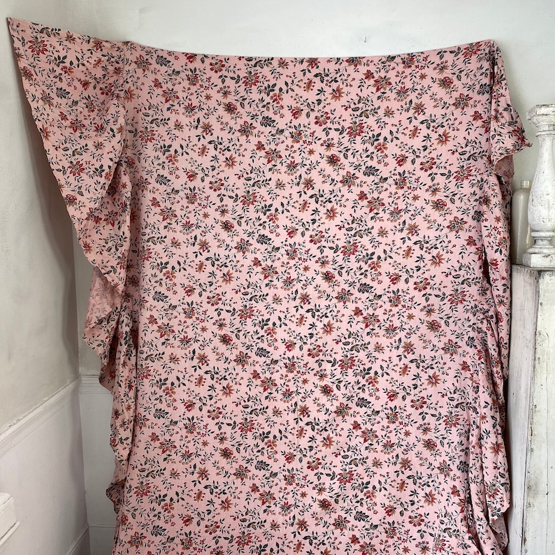May include: A pink fabric with a small floral print in shades of red, brown, and black. The fabric has a ruffled edge.