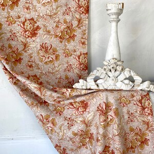 Könnte beinhalten: Ein beigefarbener Stoff mit einem floralen Muster in Braun- und Orangetönen. Der Stoff ist über ein weißes, dekoratives Holzstück gelegt.