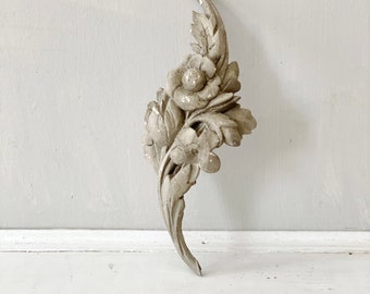 Puede incluir: Una pieza de decoración de pared blanca, adornada, de forma floral con un diseño de hojas. La pieza está hecha de yeso o un material similar y tiene un acabado desgastado.