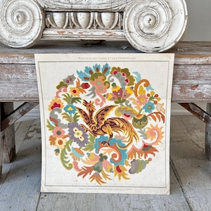 May include: A vintage needlepoint design featuring a colorful floral pattern with a stylized bird in the center. The design is framed in a white mat and has the text "Moniteur des Dames et des Demoiselles" at the top.