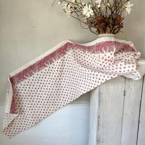 May include: A white tablecloth with a pink floral pattern. The tablecloth is draped over a white wooden cabinet.