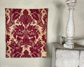 May include: A red and cream fabric with a floral pattern. The fabric is hanging on a wall next to a white painted cabinet.