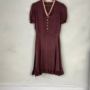 May include: A maroon vintage dress with a pink trim around the neckline and short sleeves. The dress has a button-up front and a ruffled hem.