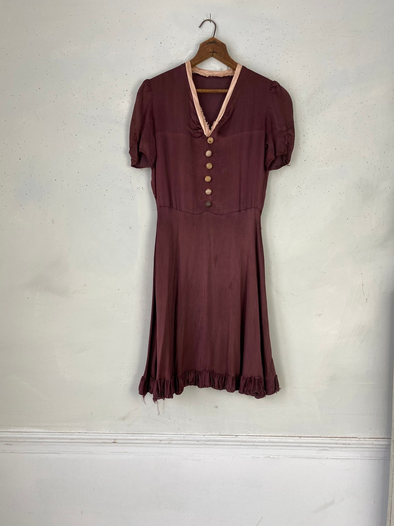 May include: A maroon vintage dress with a pink trim around the neckline and short sleeves. The dress has a button-up front and a ruffled hem.