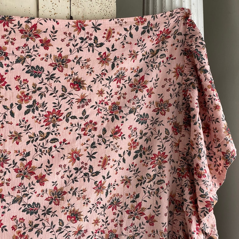 May include: Pink fabric with a floral pattern in shades of red, brown, and green. The fabric has a ruffled edge.