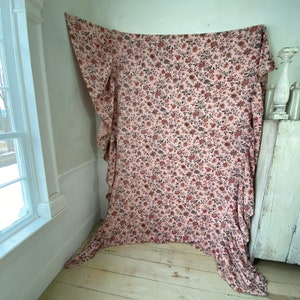 May include: A pink fabric with a floral pattern in shades of red, brown, and black. The fabric is draped over a white wall and has a ruffled edge.