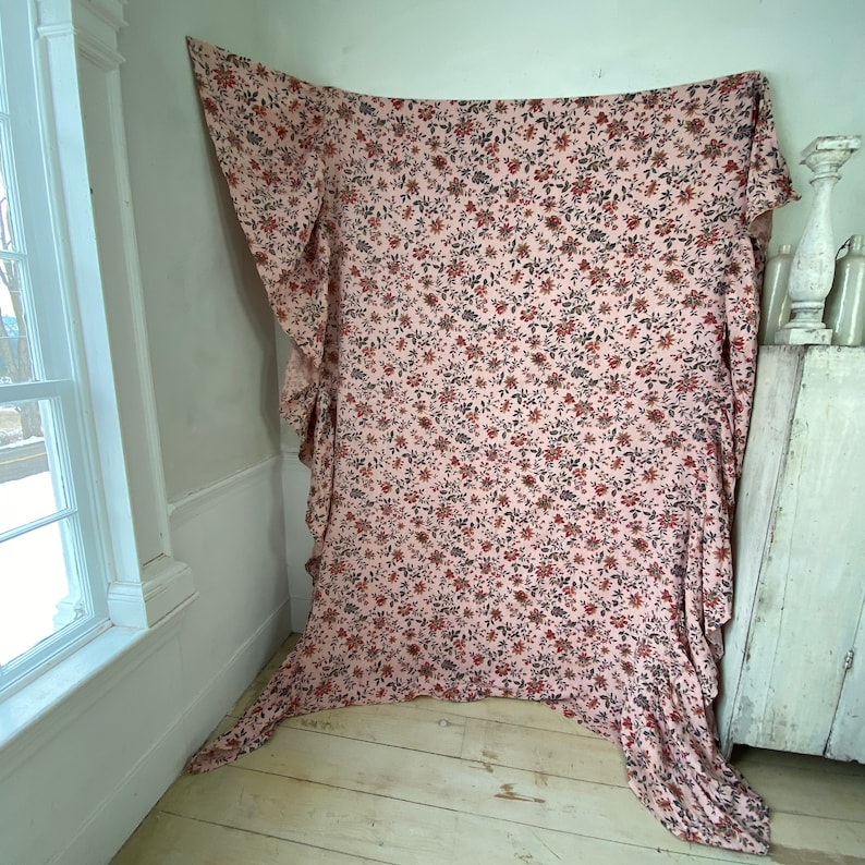 May include: A pink fabric with a floral pattern in shades of red, brown, and black. The fabric is draped over a white wall and has a ruffled edge.