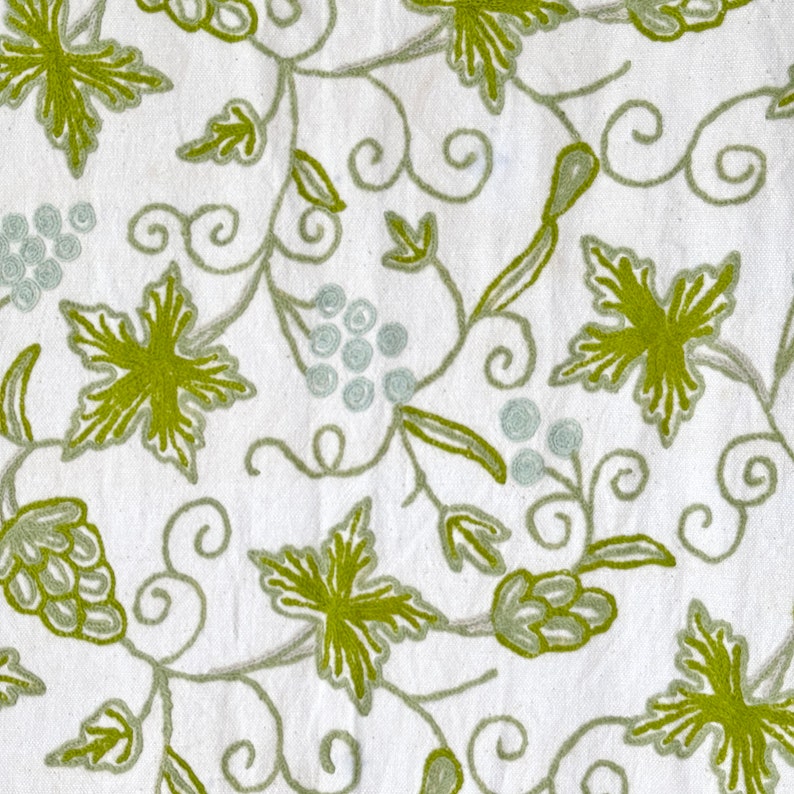 May include: White fabric with an embroidered design of green leaves and vines. The design is repeated throughout the fabric.