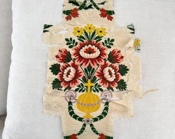 May include: A white pillow with a floral patterned fabric patch sewn on the front. The fabric patch features red, pink, yellow, and green flowers with a yellow vase and a cross in the center.