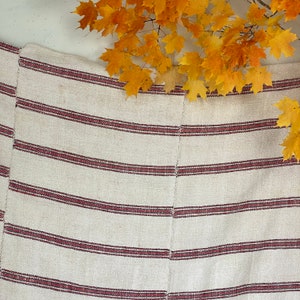 May include: A white and red striped woven fabric with a subtle texture. The fabric has a natural, rustic look and feel.