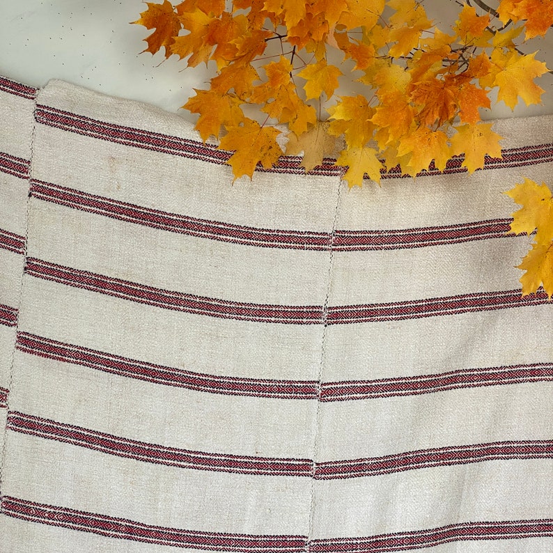 May include: A white and red striped woven fabric with a subtle texture. The fabric has a natural, rustic look and feel.