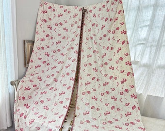May include: A pair of white curtains with a pink floral pattern and a tassel trim. The curtains are hanging from a rod and are draped over a white couch.