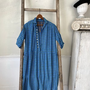 May include: A blue and green plaid dress with a button-up front and short sleeves. The dress is hanging on a wooden ladder.
