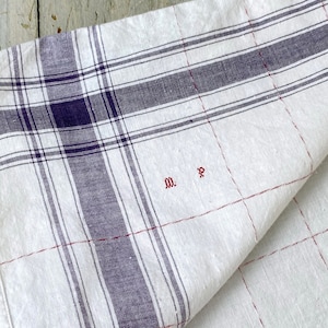 May include: White linen tea towel with a blue and red plaid pattern. The towel has the initials "M.P." embroidered in red thread.