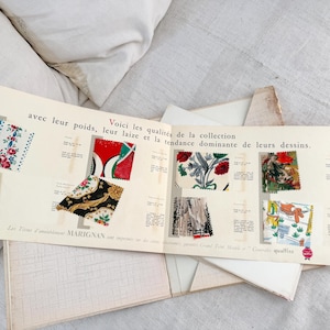 May include: A vintage Marignan fabric sample book featuring an off-white paper display with printed French text and various colorful textile swatches attached. The swatches showcase diverse floral, geometric, and illustrative patterns in red, blue, green, and black, organized with descriptive technical details for each fabric type.