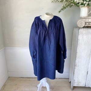 May include: A navy blue tunic top with a gathered neckline and long sleeves. The sleeves have a gathered cuff detail.