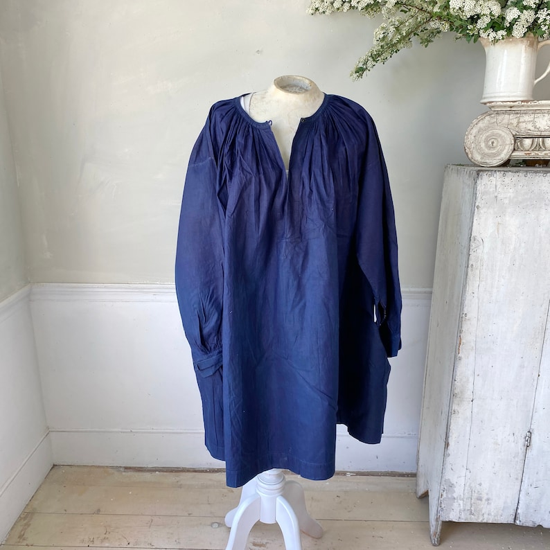 May include: A navy blue tunic top with a gathered neckline and long sleeves. The sleeves have a gathered cuff detail.