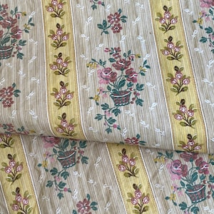 Könnte beinhalten: Beigefarbener Stoff mit gelben Streifen und einem Blumenmuster. Die Blumen sind rosa, rot und grün. Der Stoff ist in der Mitte gefaltet.